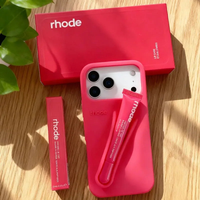 Pink Rhode phone case with accessories on a wooden surface, featuring the 'rhode' brand.
