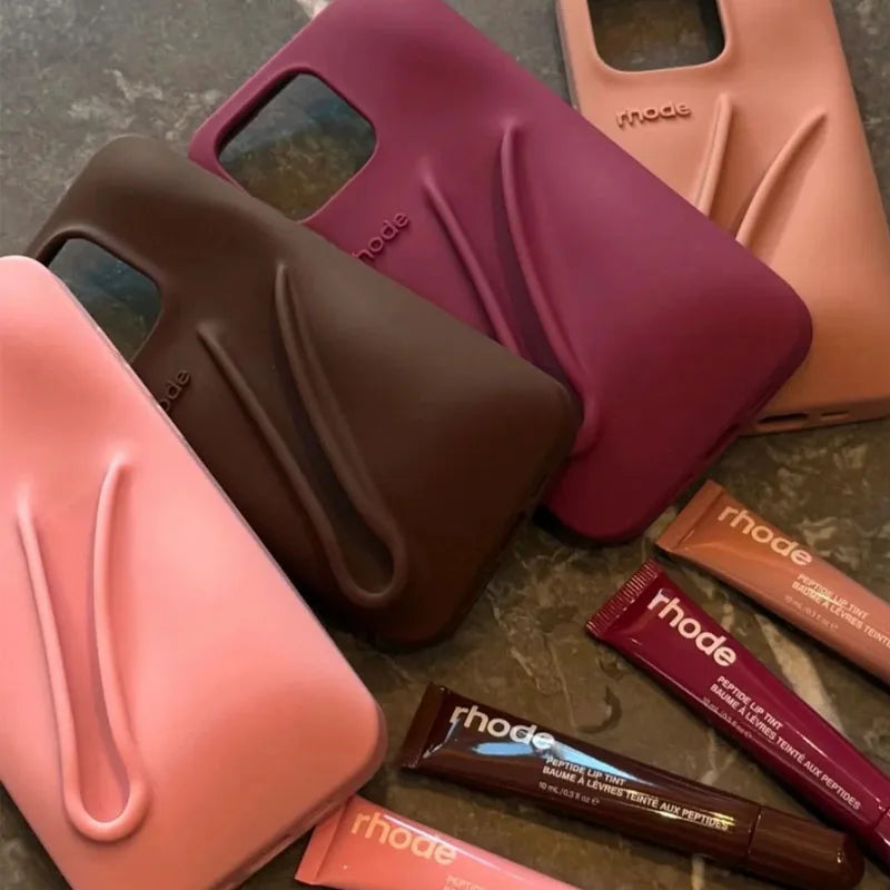 Collection of phone cases and lip products with 'rhode' branding on a textured surface.