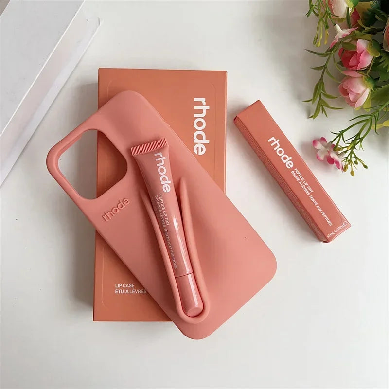 Pink phone case and lip balm set with 'rhode' branding on a white surface with flowers.