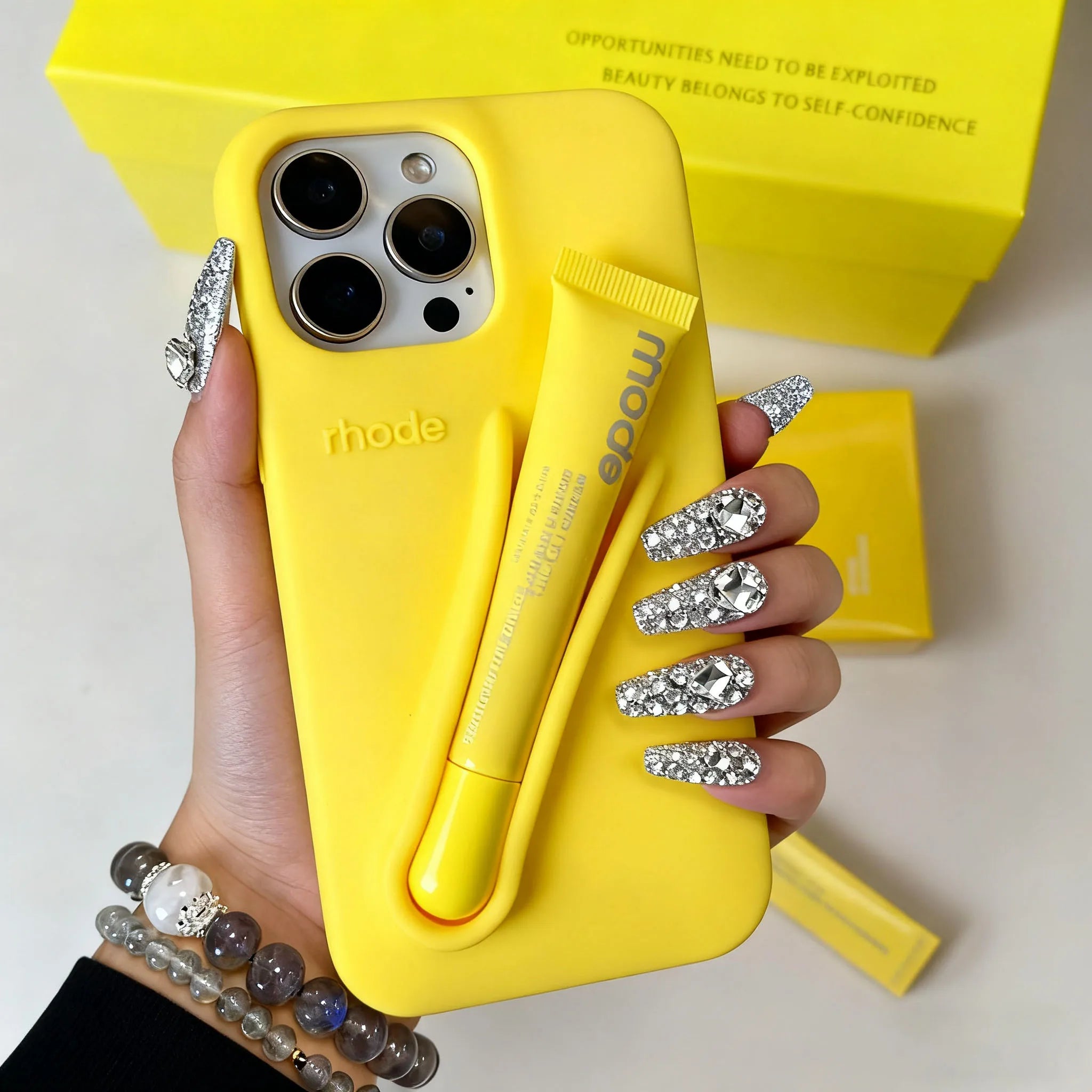 Hand holding a yellow phone case with 'rhode' branding, against a light background.