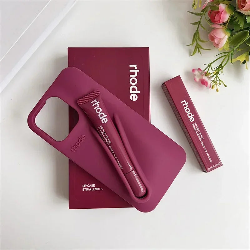Pink lip case with 'rhode' branding on a white surface with a floral arrangement.